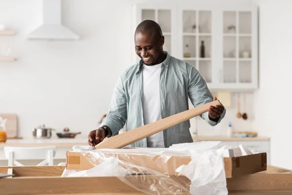 Ξεπακετάρω το νέο ξύλινο τραπέζι. Ενθουσιασμένος Αφροαμερικάνος έτοιμος να συναρμολογήσει γραφείο μόνος του μετά τη μετεγκατάσταση του σπιτιού. — Φωτογραφία Αρχείου