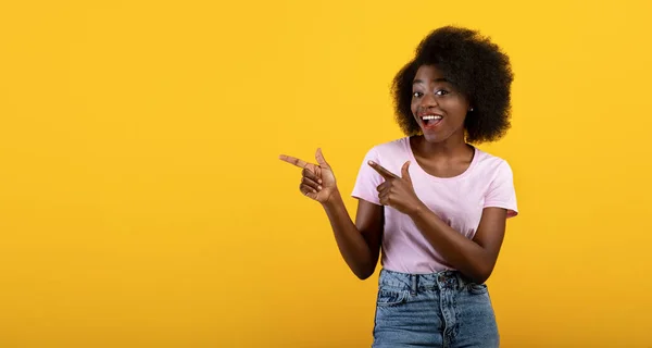 Cooles Angebot. Fröhliche afrikanisch-amerikanische Dame zeigt mit zwei Fingern zur Seite auf Kopierraum auf gelbem Hintergrund, Panorama — Stockfoto
