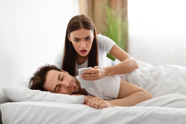 Esposa leyendo mensaje en el teléfono mientras infiel marido durmiendo en el interior — Foto de Stock