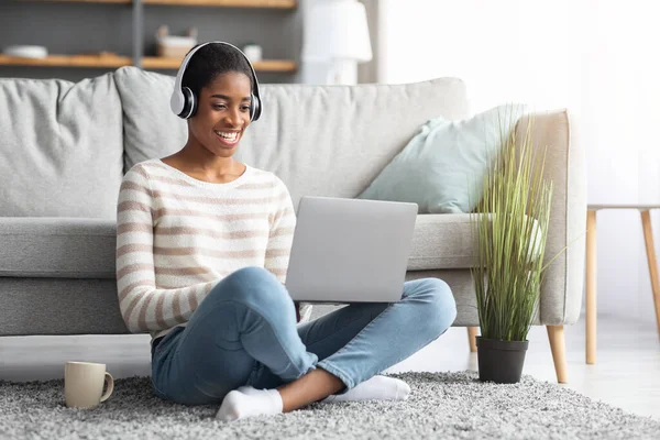 Joven dama negra en auriculares inalámbricos Estudio con portátil en casa —  Fotos de Stock