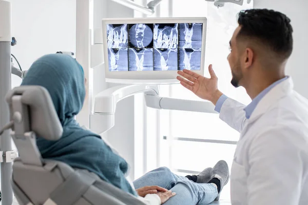 Άραβας άντρας οδοντίατρος που δείχνει το αποτέλεσμα της θεραπείας στην ακτινογραφία δοντιών στο μουσουλμάνο ασθενή — Φωτογραφία Αρχείου