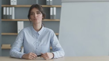 Resmi giyinmiş, kameraya konuşan, online sunum yapan kendine güvenen genç bir kadının portresi.