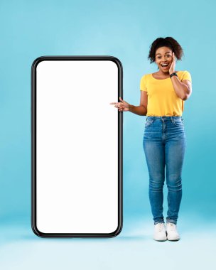 Havalı Afro kadın, ekranda yeni mobil uygulama için yeri olan akıllı telefona işaret ederek harika bir teklif sunduğuna inanamıyor.