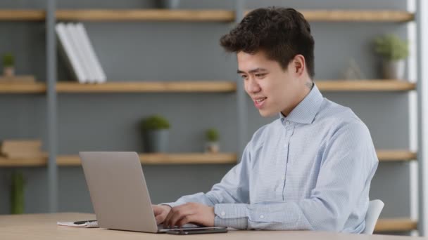 Młody azjatycki kierownik biura pracuje na laptopie, czyta e-maile z informacjami i świętuje sukces — Wideo stockowe
