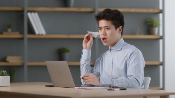 Fim da semana de trabalho. Jovem positivo asiático trabalhador de escritório fazendo e jogando avião de papel, relaxante no local de trabalho — Vídeo de Stock