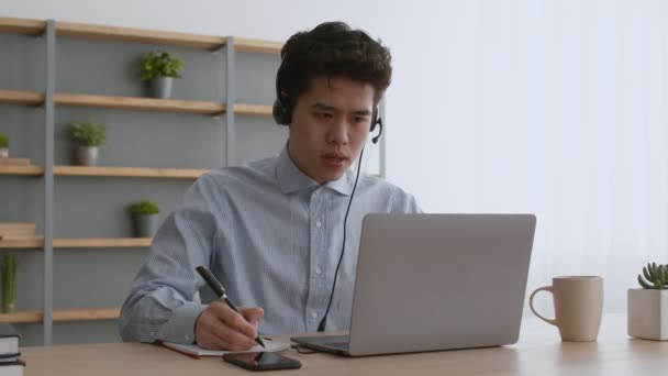 Segélyhívó központ. Fiatal ázsiai srác operátor headset video chat az ügyféllel, és megvitatása hiba részleteit — Stock videók