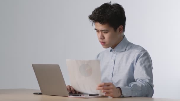 Jeune homme d'affaires asiatique concentré lisant des documents financiers avec un tableau de projet et réfléchissant à la stratégie d'entreprise — Video