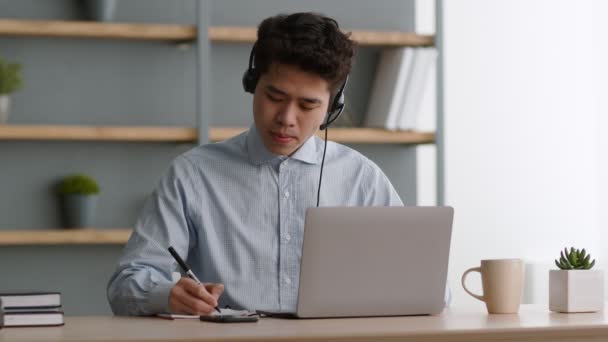 Jeune homme asiatique opérateur de centre d'appels dans casque parler au client par chat vidéo et en notant toutes les suggestions — Video