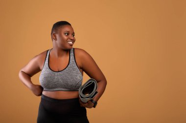 Şişko zenci kadın yoga minderini tutuyor, yan bakıyor.