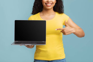 Özelleştirilmiş web sitesi ve online reklam. Genç Afro-Amerikalı kadın boş ekran ve ekinle dizüstü bilgisayarı işaret ediyor.