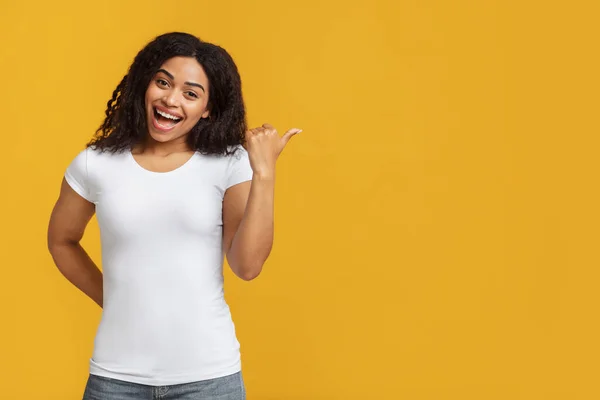 Fröhliche schwarze Frau zeigt zur Seite, zeigt freie Fläche für Ihr Design oder Ihre Werbung, gelber Hintergrund — Stockfoto