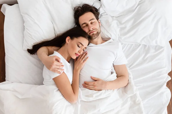 Couple marié dormant embrassant dans un lit confortable à l'intérieur, vue sur le dessus — Photo