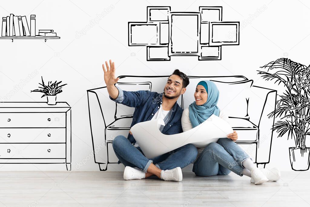 Happy arab husband and wife in hijab planning house interior