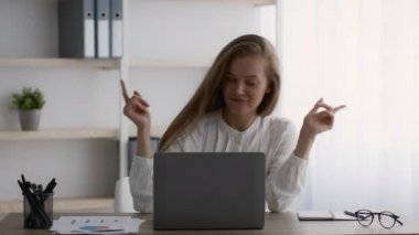 Ofiste dizüstü bilgisayarla çalışırken işyerinde dans eden genç bir kadın.