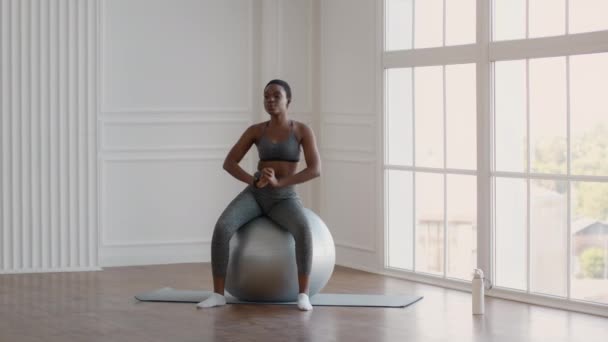 Ajuste a jovem senhora negra se exercitando com Fitball em casa, girando seus quadris — Vídeo de Stock