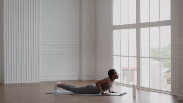 Joven mujer afroamericana practicando yoga, haciendo ejercicio de cobra en la estera de fitness — Vídeos de Stock