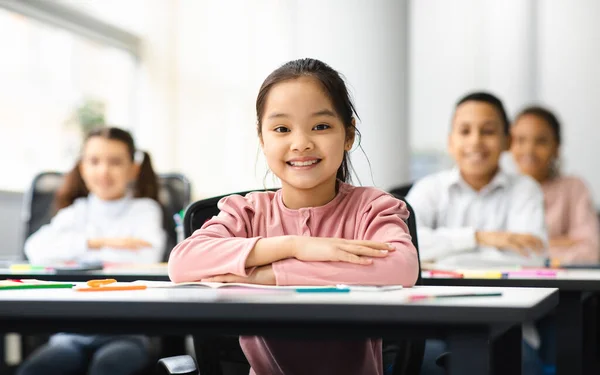 Egy kis ázsiai lány portréja, aki az asztalnál ül az osztályteremben. — Stock Fotó