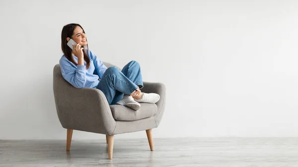 Vänlig tusenårig kvinna talar på mobiltelefon, sitter i fåtölj, enjoyng samtal med vän — Stockfoto
