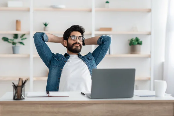 Ragazzo arabo freelance di successo che riposa tenendosi per mano dietro la testa, rilassarsi sul posto di lavoro dopo il lavoro online — Foto Stock