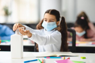 Kadın öğrenci ellerinde antibakteriyel dezenfektan uyguluyor.