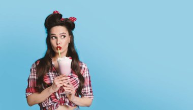 Eski moda kıyafetli seksi bir kadın portresi. Milk shake içiyor. Mavi arka planda boş bir alana bakıyor.
