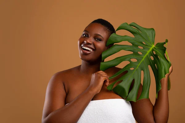 Retrato de hermosa mujer afroamericana con curvas sosteniendo hoja de monstera —  Fotos de Stock