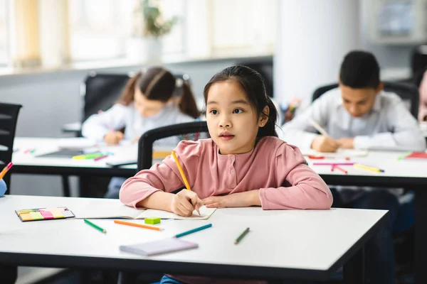 Portré kis ázsiai lány ül az osztályteremben, és írás — Stock Fotó