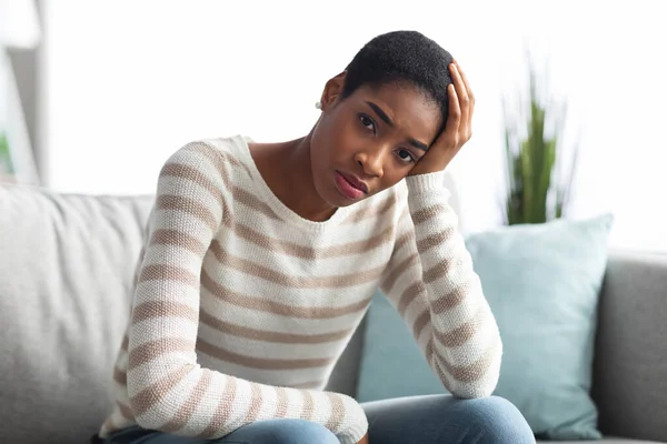 Retrato de mujer negra trastornada sentada en un sofá y mirando a la cámara —  Fotos de Stock