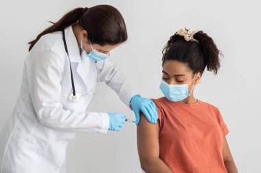 Beyaz iş elbiseli hemşire siyah kadın için aşı yapıyor.
