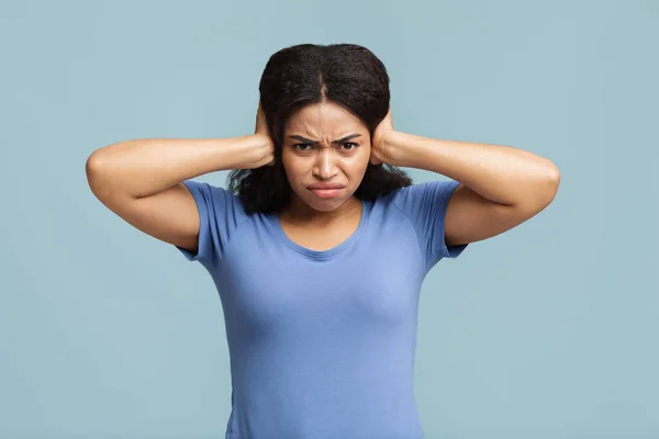 Aufgebrachte afrikanisch-amerikanische Frau schließt ihre Ohren mit den Händen, um sich vor lauten Geräuschen auf blauem Studiohintergrund zu schützen — Stockfoto