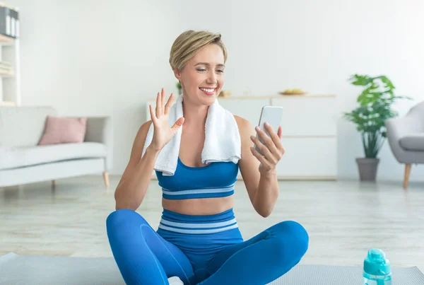 Smiling woman exercising and waving at smartphone screen — Stock Photo, Image