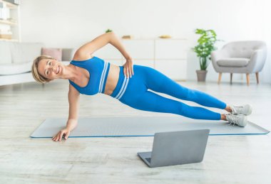 Orta yaşlı bir kadın bilgisayarla yan tahtada yatıyor.