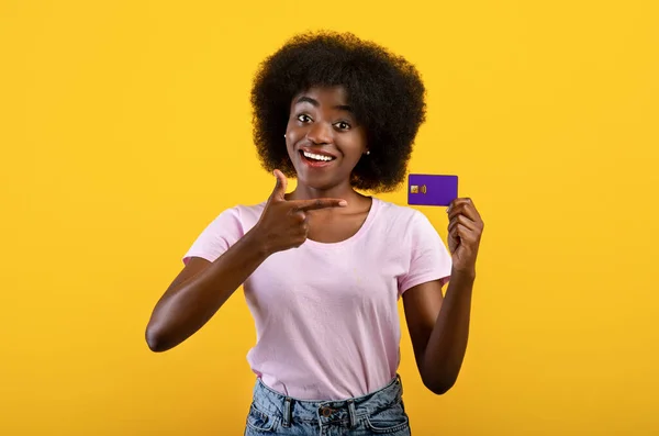 Positiver afrikanisch-amerikanischer Bankkunde zeigt Kreditkarte, empfiehlt Bankdienstleistungen, gelber Hintergrund — Stockfoto