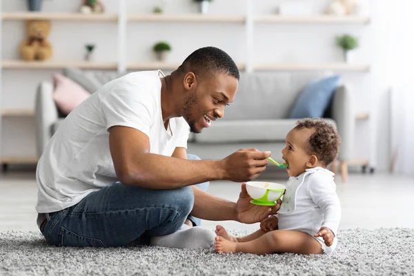 A los padres les importa. amar negro papá alimentación su lindo bebé hijo en casa — Foto de Stock