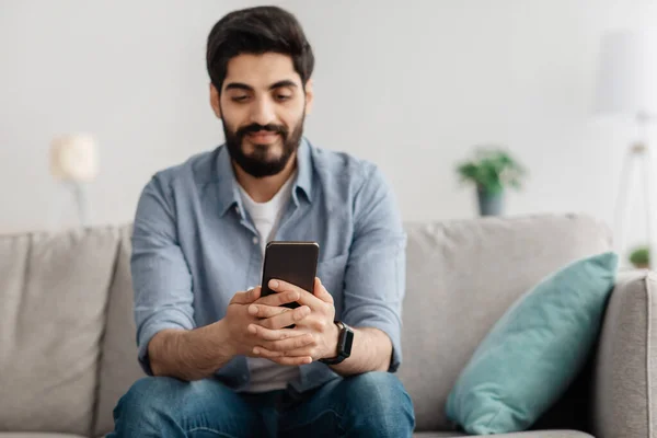 Primer plano del tipo árabe en traje casual usando un teléfono inteligente moderno, descansando en el interior del hogar, espacio para copiar — Foto de Stock