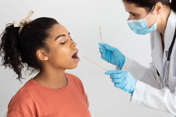 Infirmière prélevant un écouvillon oral pour un échantillon de coronavirus chez une femme noire — Photo