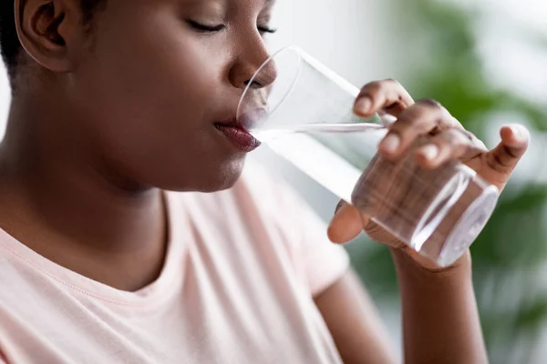 Păstrați hidratat pentru o viață mai sănătoasă. O femeie neagră supraponderală care bea apă minerală limpede din sticlă în interior — Fotografie, imagine de stoc