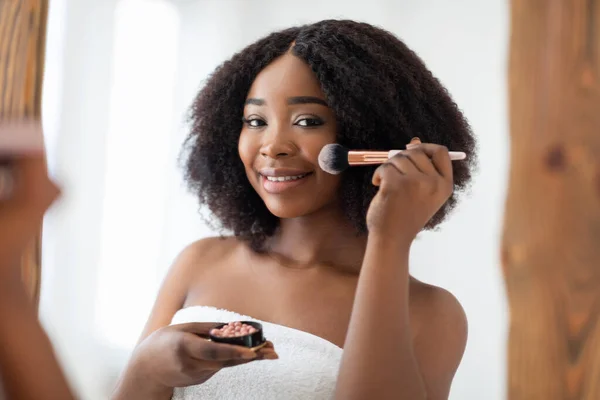 Conceito de maquiagem natural. Encantadora senhora preta aplicando blusher ou pó na frente do espelho em casa — Fotografia de Stock