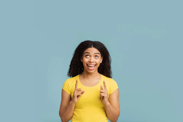 Interessantes Angebot. Fröhliche schwarze Frau zeigt auf freien Raum über ihrem Kopf, steht über blauem Hintergrund — Stockfoto