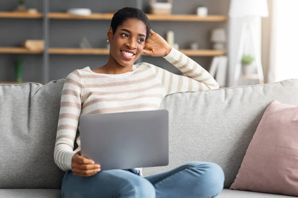 Hermosa mujer afroamericana feliz joven relajante en casa con computadora portátil —  Fotos de Stock