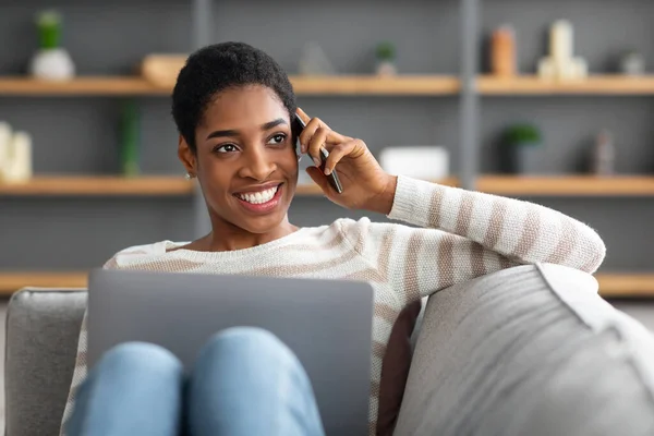 Comunicazione remota. nero donna utilizzando computer portatile e parlando su cellulare a casa — Foto Stock