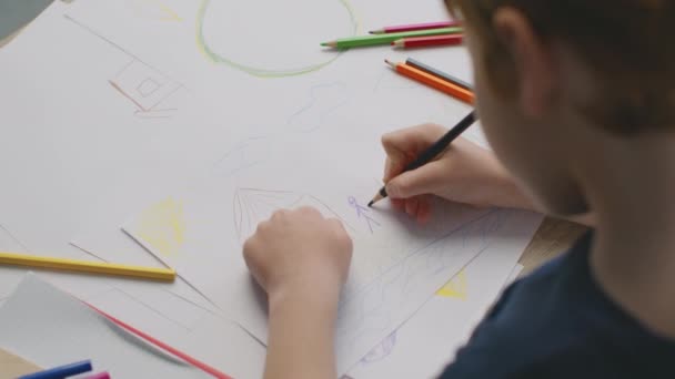 Концепция детской психологии. Вид сверху на неузнаваемого маленького мальчика дошкольного возраста, рисующего картину счастливой семьи возле дома — стоковое видео