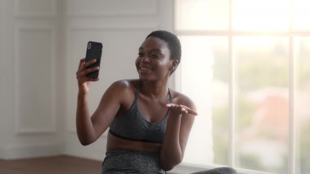 Młoda Afrykanka w odzieży sportowej Dokonywanie połączeń wideo na smartfonie w domu — Wideo stockowe