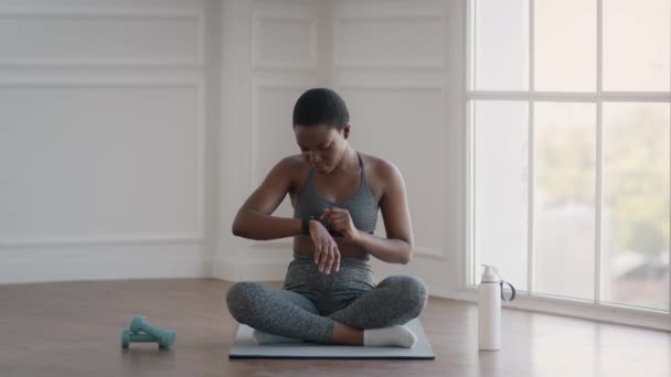 Deportiva mujer negra chequeando actividad de fitness en smartwatch después de entrenar en casa — Vídeos de Stock