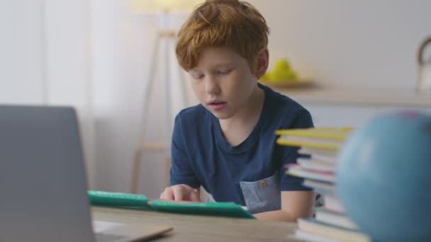 Пора учиться. Милый рыжий мальчик читает дома книги, готовится к школе, изучает иностранный язык дистанционно — стоковое видео