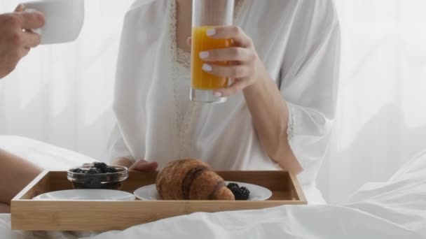 Casal tomando café da manhã na cama, mulher bebendo suco e homem tomando café — Vídeo de Stock