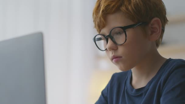 Primer plano retrato de pequeño pelirrojo enfocado escribiendo en el ordenador portátil, estudiando en línea distante de casa — Vídeo de stock