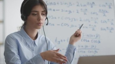Çevrimiçi eğitim kavramı. Öğrencilere video konferansı yoluyla matematik formüllerini açıklayan kulaklık takan genç bir bayan öğretmen.