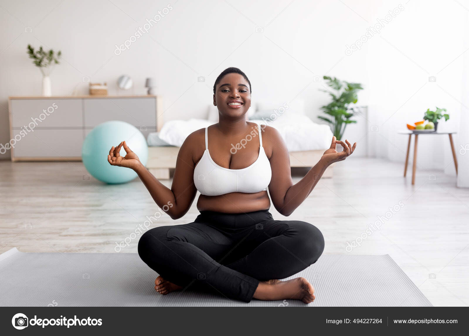 Overweight black woman sitting on sports mat in lotus pose