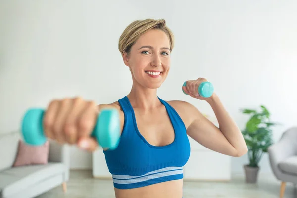 Lächelnde Frau mittleren Alters trainiert zu Hause mit zwei Kurzhanteln — Stockfoto